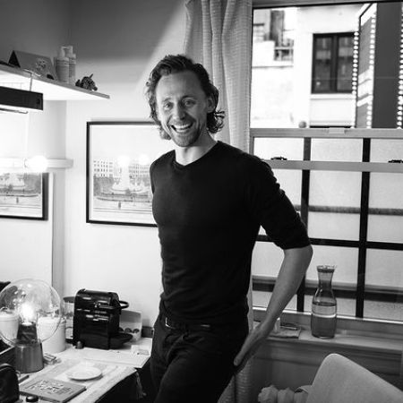 Tom Hiddleston wears a black T-shirt while posing for a picture